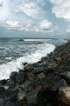 a pebbled beach on a bright day with calm sea waves splashing against the pebbles as a background