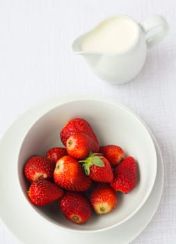 A bowl of ripe strawberries with a jug of cream in the background