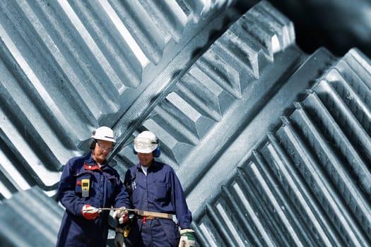 two engineers, workers, standing in front of gears and cogs machinery