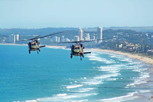 Australian Army Black choppers fly North across Surfers Paradise and Gold Coast beaches Australia.