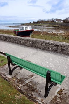 a green metal bench with a view of an old boat in a bay in ireland
