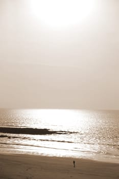 sunshine reflected on a golden beach with jogger of the west coast of ireland in sepia