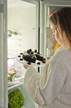 young woman getting cake out of the fridge