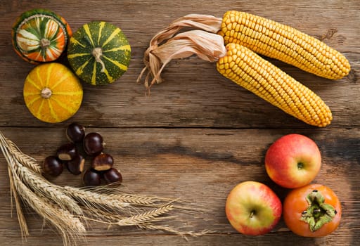 Pumpkins, corn, chestnuts, apple and persimmon fruit on wooden background