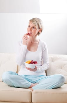 Young blond woman eating fruit on the sofa
