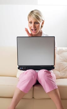 Young blond upset woman with laptop on sofa