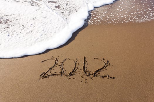 2012 written in sand on beach with sea waves starting to erase the word