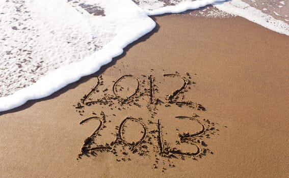 2012 and 2013 written in sand on beach with sea waves starting to erase the word
