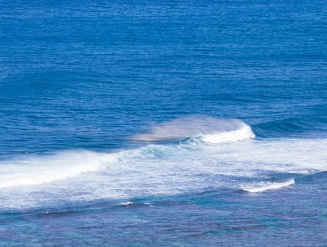 Waves crashing on reef of coast of Kauai and forming rainbow colors in the spray