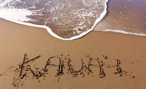 Kauai written in sand on beach with sea waves starting to erase the word