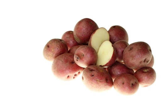 Fresh small red potatoes with one cut in half on top in front of a white background.
