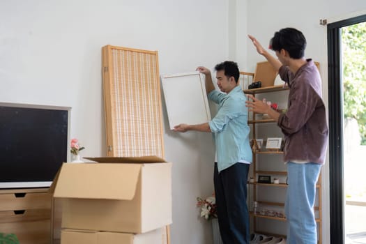 A joyful gay couple unpacks and arranges furniture in their new house, illustrating teamwork and shared joy in their new space.