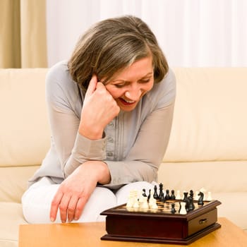Senior woman play chess happy sit alone on sofa