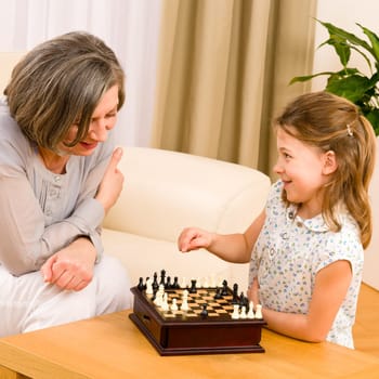 Young girl playing chess with grandmother together at home