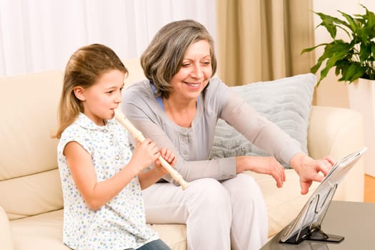 Grandmother teach young girl to play flute happy sitting on sofa