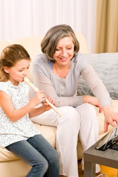 Grandmother teach young girl to play flute happy sitting on sofa