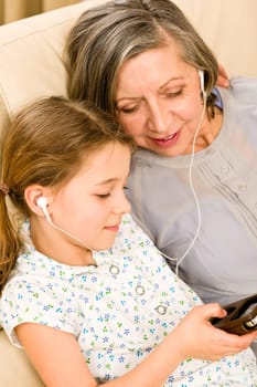 Granddaughter and grandmother listen to MP3 music headphones together smiling