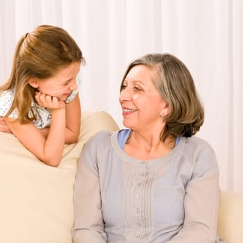 Grandmother and granddaughter look at each other relax on sofa