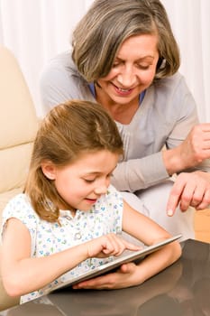 Grandmother with young girl use touch screen tablet computer smiling