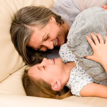 Grandmother with granddaughter hugging smiling together lying on sofa