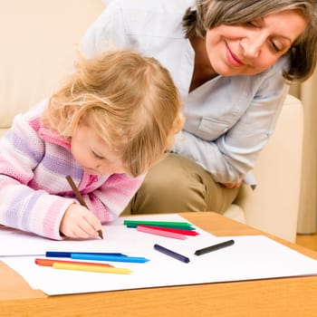 Grandmother and little girl drawing together with pencils at home