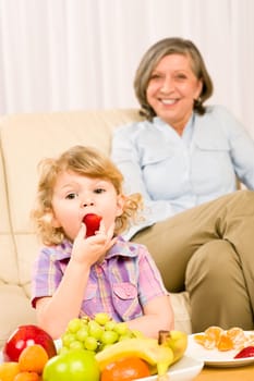 Little girl eat strawberry fruit with grandmother relaxing on sofa