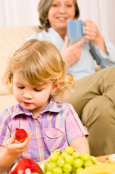 Little girl eat strawberry fruit with grandmother relaxing on sofa