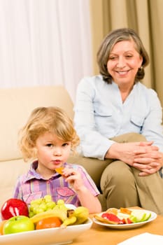 Little girl eat apricot fruit with grandmother relaxing on sofa
