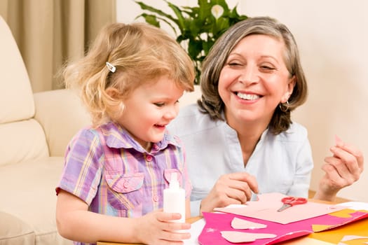Grandmother with granddaughter playing together glue hearts on paper