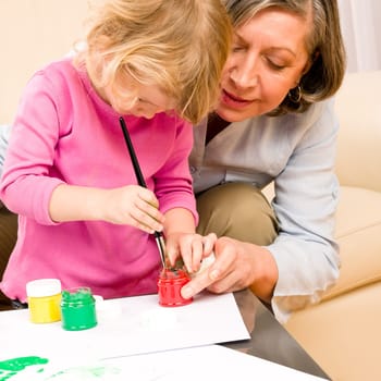 Grandmother with granddaughter playing together paint handprints on paper