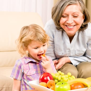 Little girl eat apricot fruit with grandmother relaxing on sofa