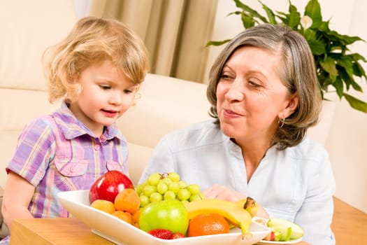 Grandmother with little granddaughter eating fruit happy together at home