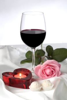 red wine with heart shaped candle on silk close up