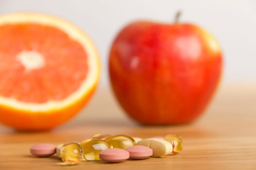 Dietary supplements are in front of a halved orange and an apple