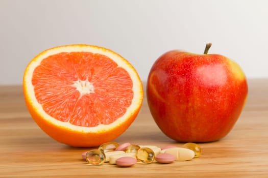 Tablets lie on a table in front of a halved orange and an apple