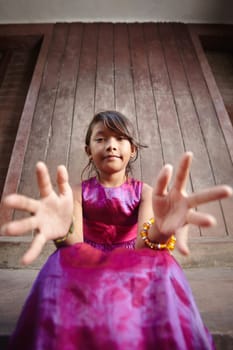 Portrait of cute Asian female child in pink dress pointing hands at camera