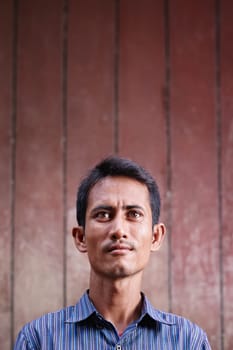 Portrait of mid adult asian man looking up against brown wall. Copy space