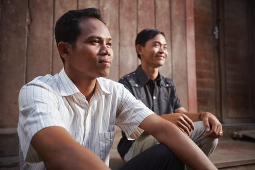 Two male cambodian friends sitting and looking away