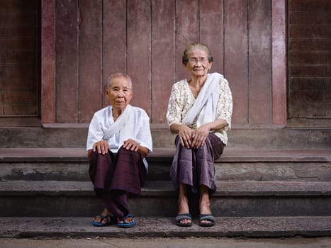 Portrait of two old asian women sitting on steps out of their house and looking at camera