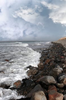 a pebbled beach on a bright day with calm sea waves splashing against the pebbles as a background