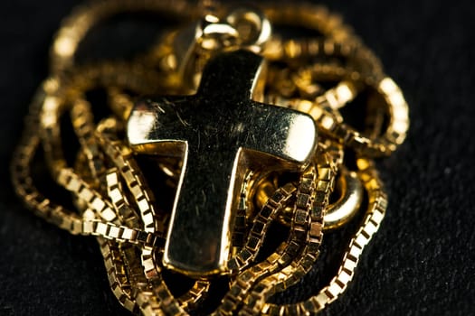 Golden jewelry cross with necklace on black fabric