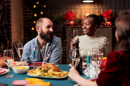 Young person raising glass for speech during christmas eve holiday at home, gathering with friends and family to eat traditional homemade food and give toast at table. Festive people.