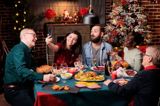 Persons enjoying photos on christmas eve festivity, celebrating december holiday together around the table. Making selfies and pictures during dinner event, having fun with smartphone.