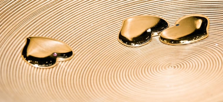 Three golden heart objects in a wooden plate. Betrayal, jealousy, concept.