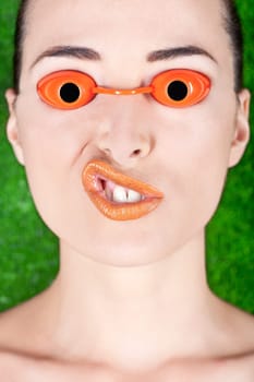 Closeup of a beautiful woman wearing tanning bed glasses and pulling a strange face isolated on green