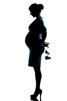 beautiful caucasian pregnant woman holding baby shoes in silhouette on studio isolated white background