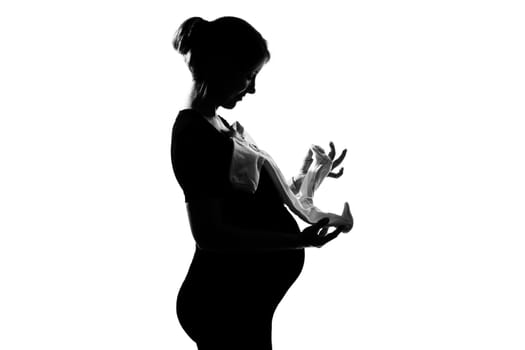 one beautiful caucasian pregnant woman holding baby clothes in silhouette on studio isolated white background