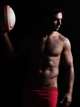 one caucasian sexy topless man portrait holding  a rugby ball on studio black background