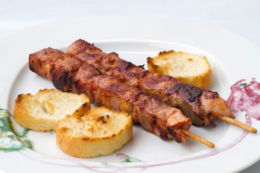 Grilled meat (kebabs) on white plate with three slices of toast