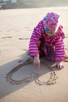 Cute little girl drawing a heart in sand with hands